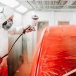 addetto della carrozzeria che passa la vernice su un auto riparata